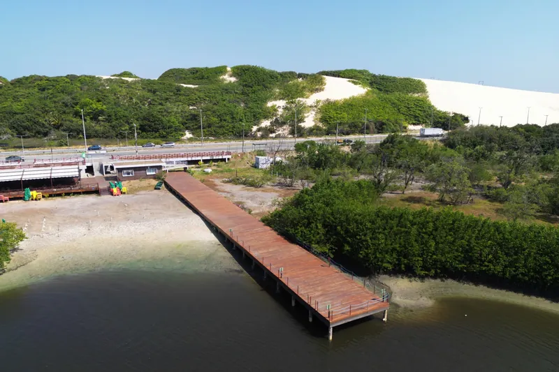 Píer de madeira sobre o rio Cocó com dunas ao fundo